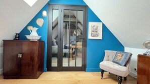 A room with a sloped ceiling, a wooden cabinet, a chair, and a door with a glass panel.