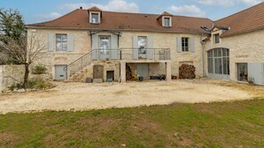 A two-story stone house with a balcony, a small attached garage, and a gravel driveway.