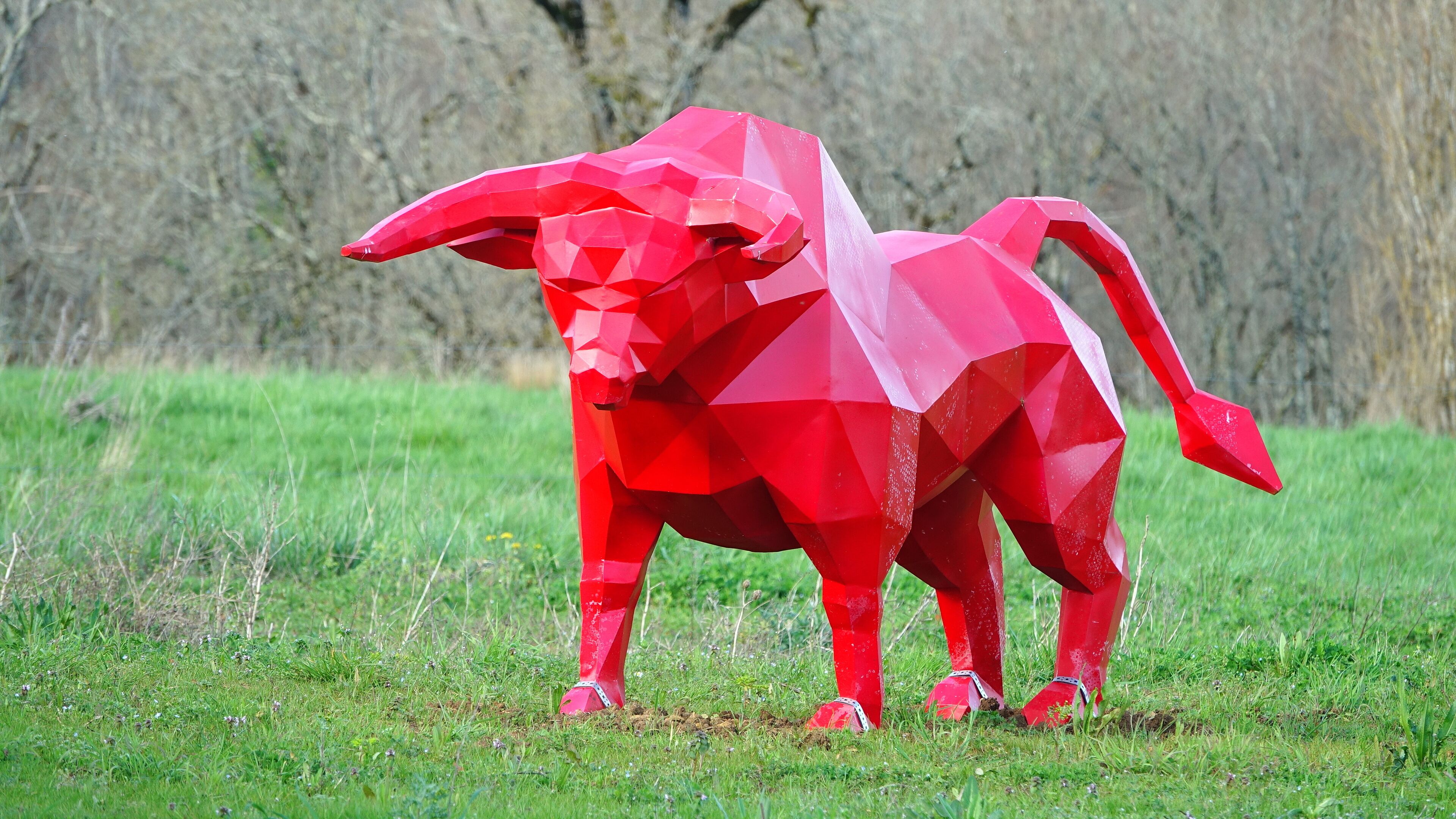 Une sculpture géométrique rouge représentant un animal, située dans un champ d’herbe.