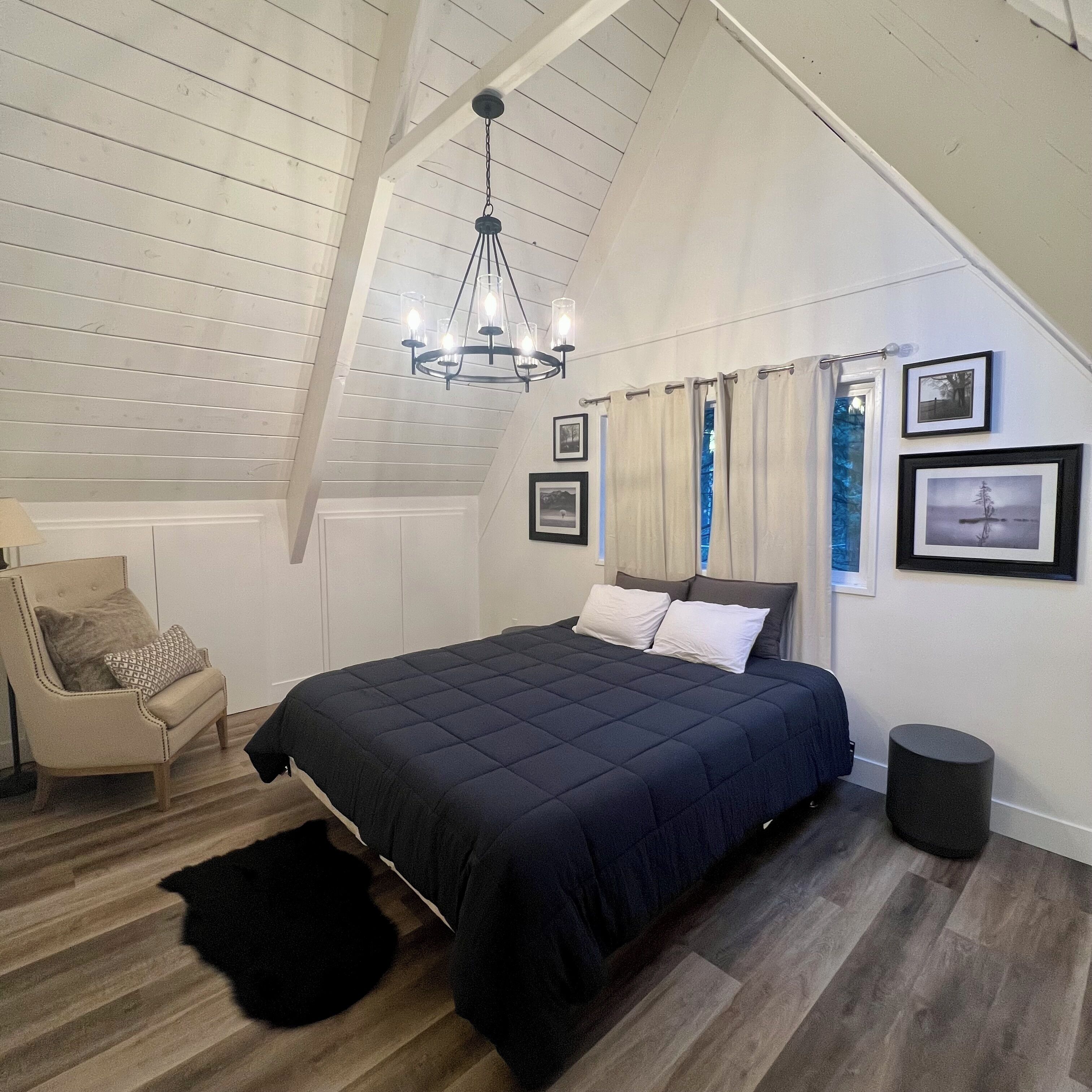Une chambre à coucher avec un lit, une chaise, un tapis noir, un lustre et des tableaux encadrés accrochés au mur.