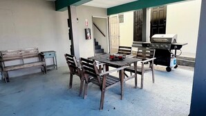 Een terras buiten met een houten tafel en stoelen, een barbecue en een trap naar een hoger gelegen niveau.