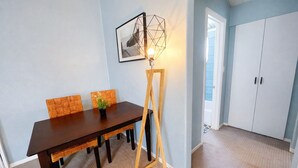 Een eetgedeelte met een donker houten tafel, twee gestreepte stoelen, een vloerlamp en een ingelijste foto aan de muur.