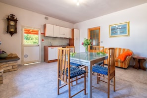 A kitchen with white cabinets, a dining table with chairs, a clock, and a window.