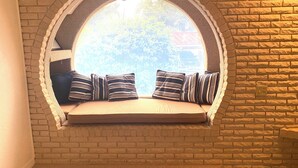 A cozy reading nook with a cushioned bench and striped pillows, set against a brick wall with a large arched window overlooking a tree. - Lake Placid Vacation Destination for the whole family! (Lake Placid)