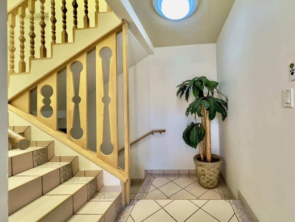 Un escalier avec des balustrades en bois, une plante en pot et un interrupteur sur le mur.