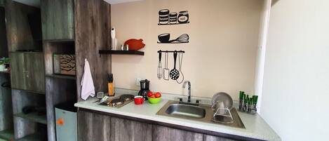 A compact kitchen with a wooden cabinet, a sink, and a countertop. There are kitchen utensils and a coffee maker on the counter.