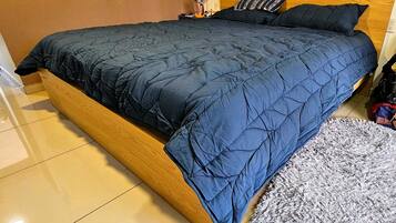 A bed with a dark blue quilt, a wooden headboard, a small table with a lamp, and a grey shaggy rug.