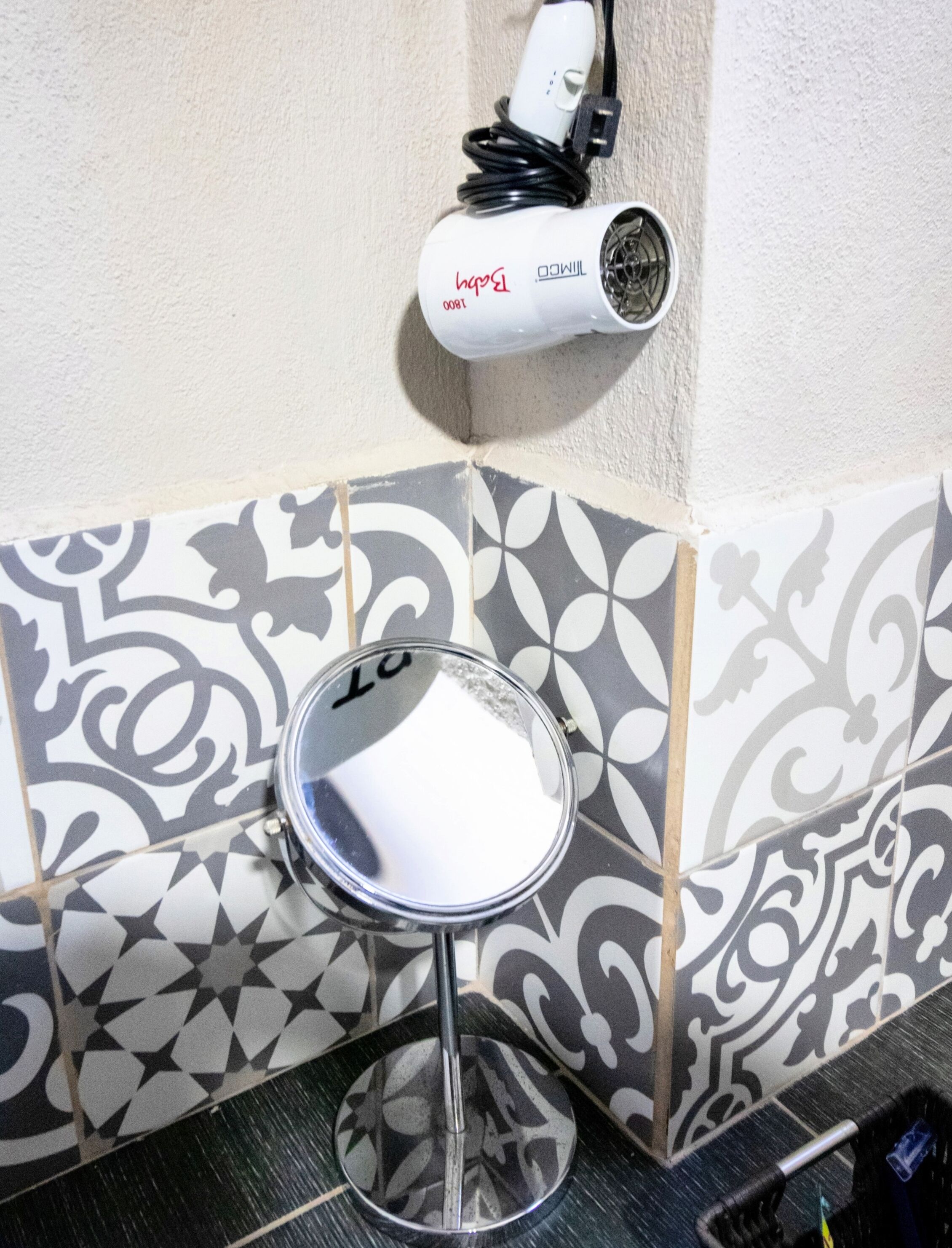 Un baño con baldosas estampadas, un espejo y un secador de pelo en la pared.