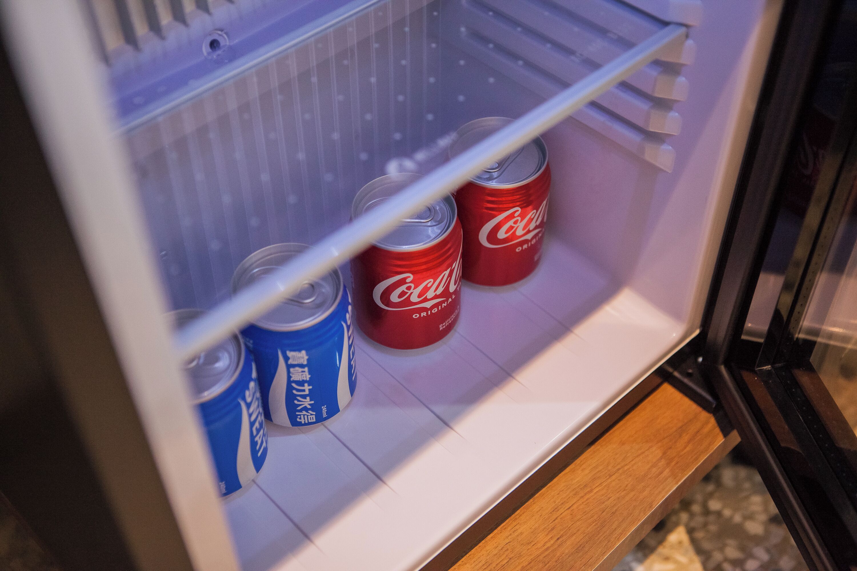 A refrigerator with two cans of Coca-Cola and one can of Sprite.