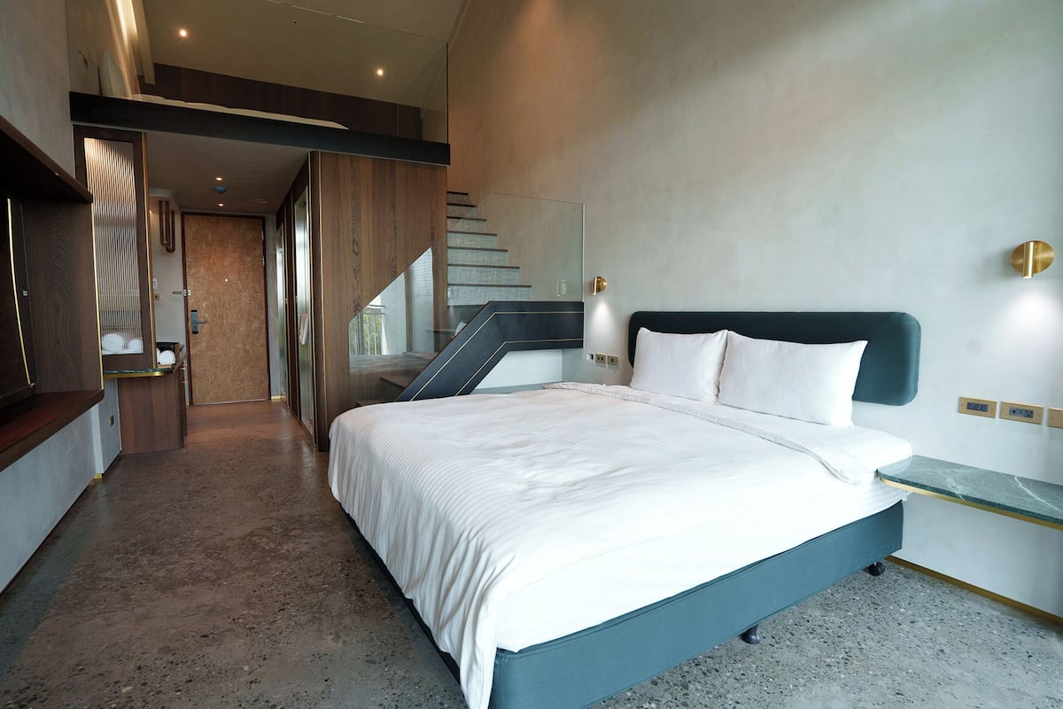 A modern bedroom with a large bed, a built-in bench, a staircase, and a minimalist design.