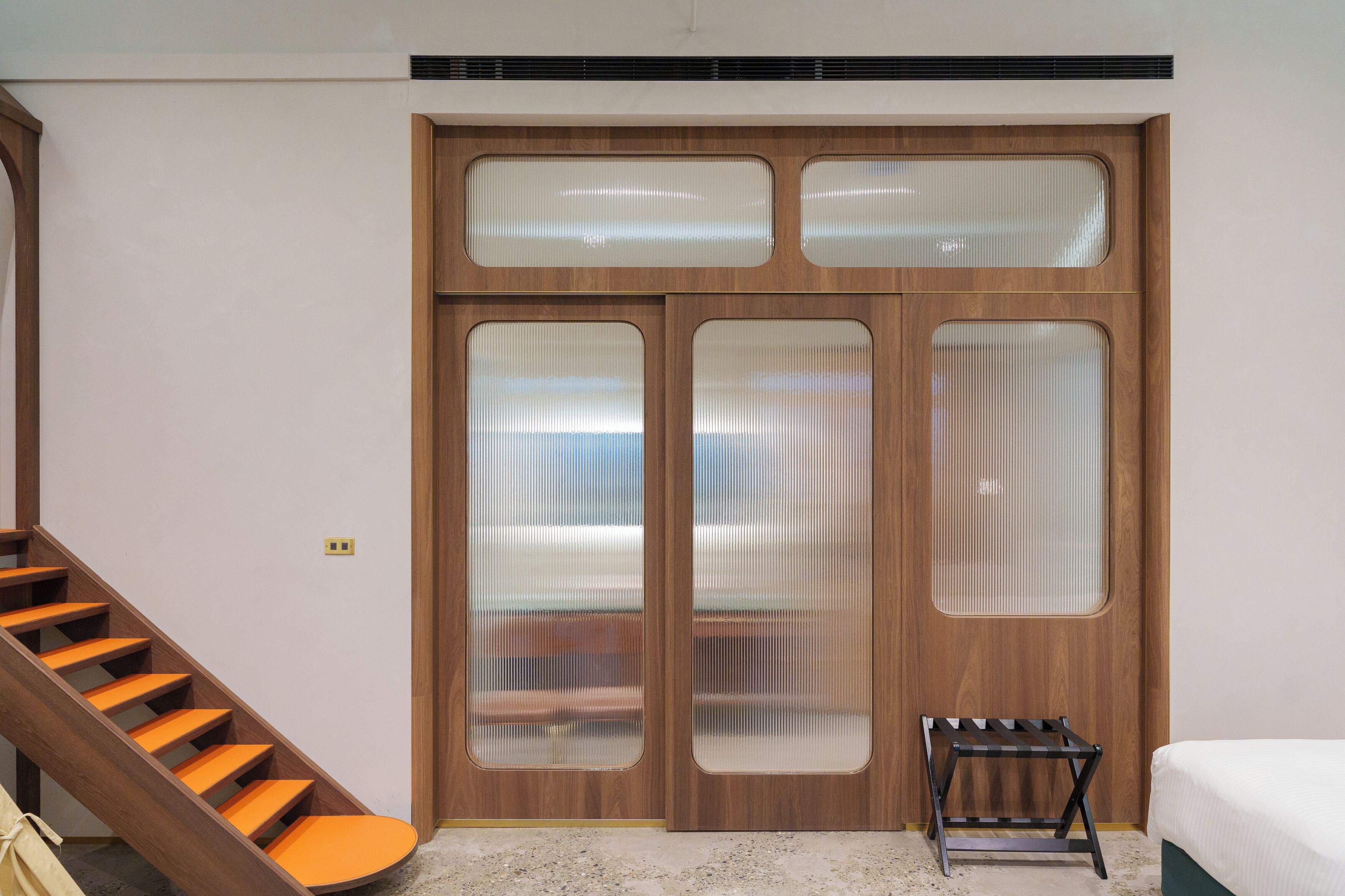 A room with a wooden staircase, a bed, and a wardrobe with frosted glass panels.