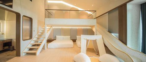 Una habitación de hotel moderna con piso de madera, una cama con ropa blanca, una escalera y un pequeño rincón de descanso con dos almohadas blancas.