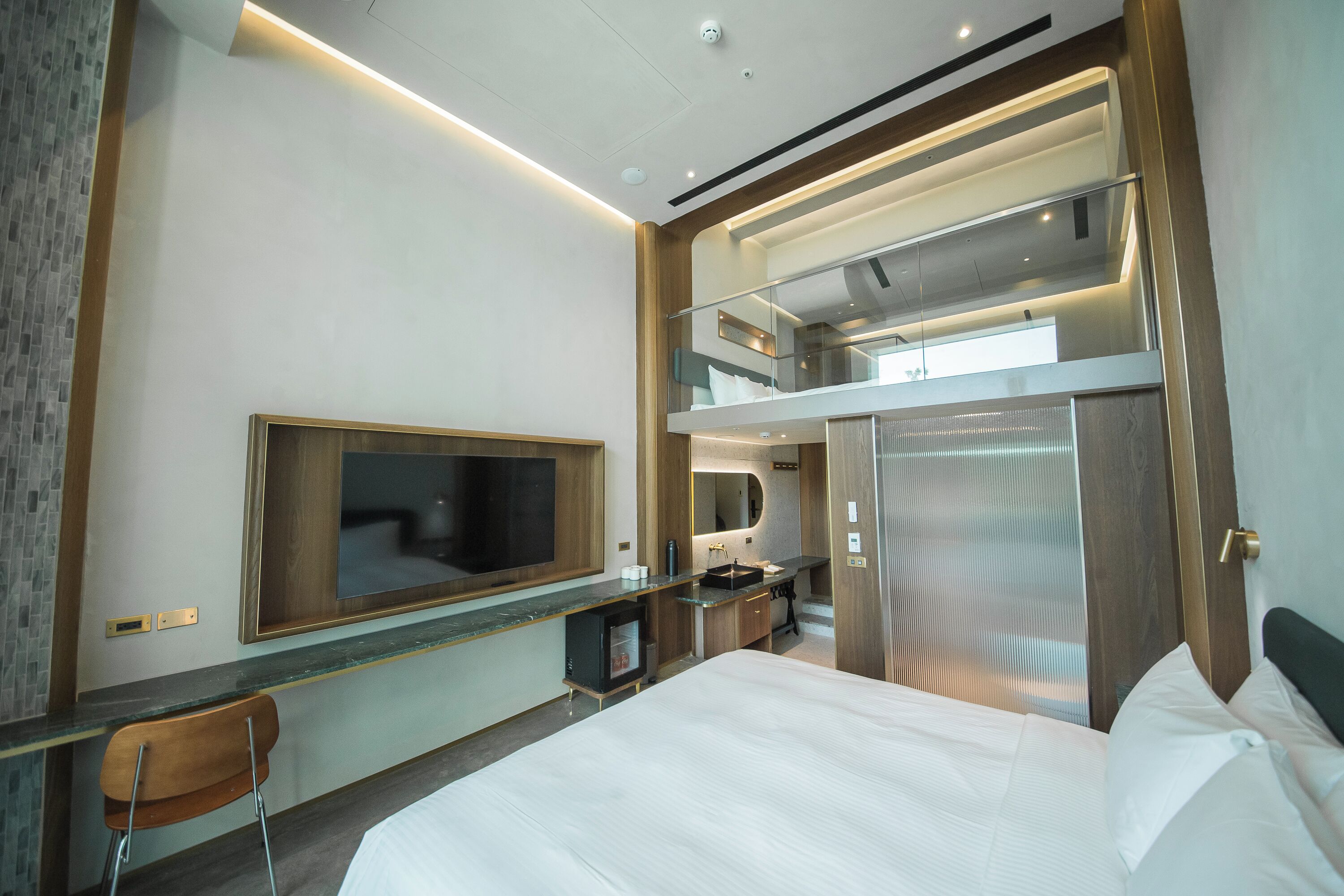 Une chambre d’hôtel moderne dotée d’un grand lit, d’un bureau avec une chaise, d’un téléviseur fixé au mur et d’un balcon avec une rambarde en verre.