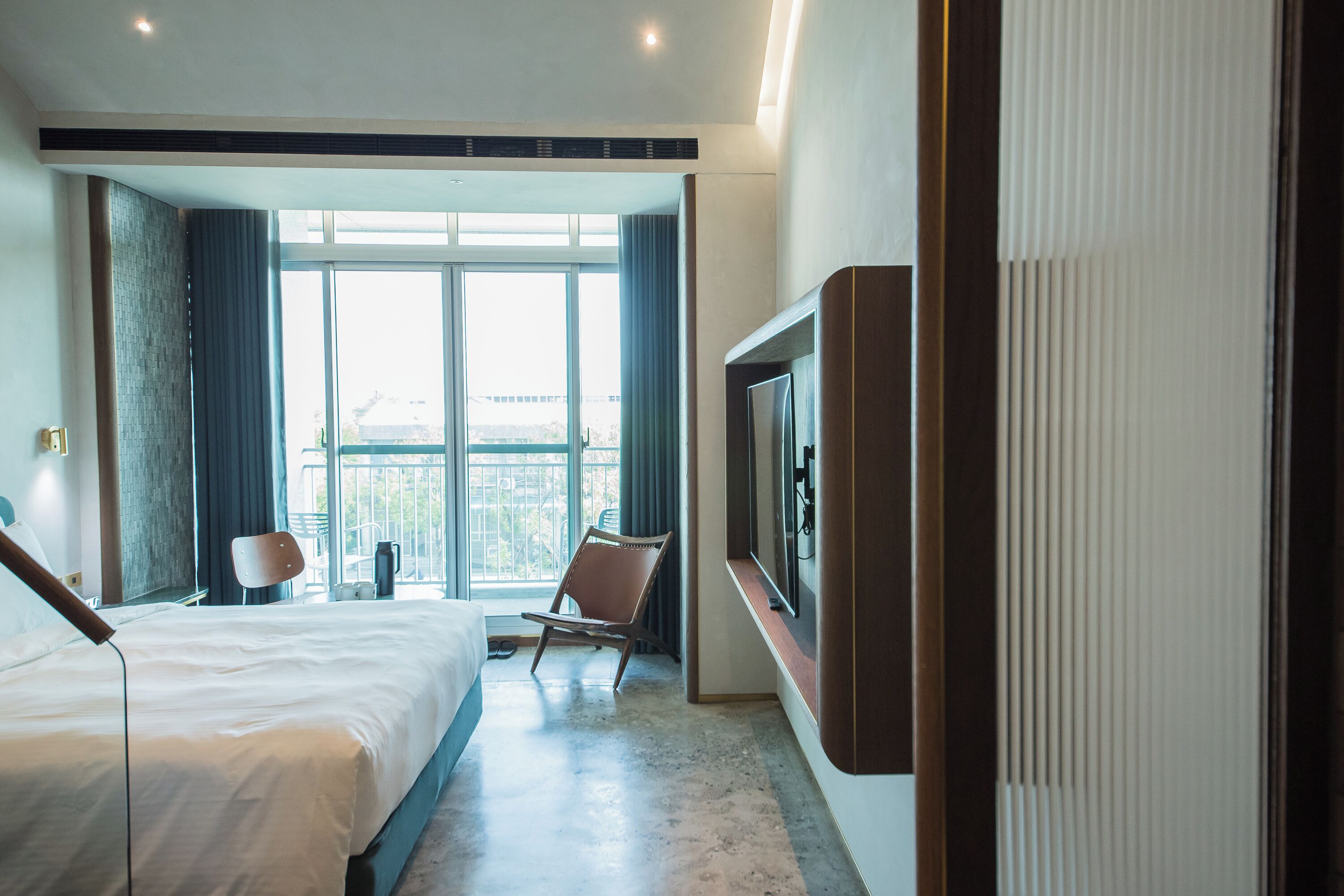 Une chambre d’hôtel avec un grand lit, une chaise, un téléviseur fixé au mur et une vue sur la ville par la fenêtre.