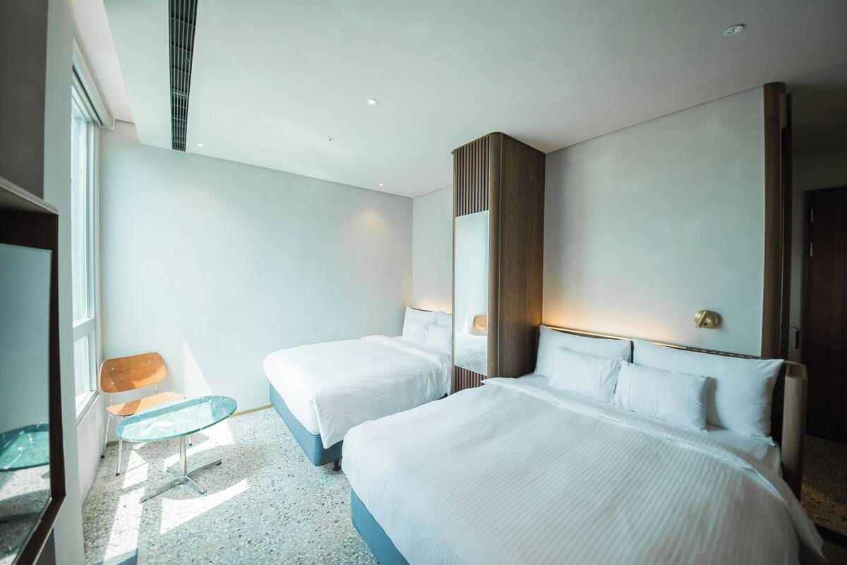 A hotel room with two beds, a small table, and a chair.
