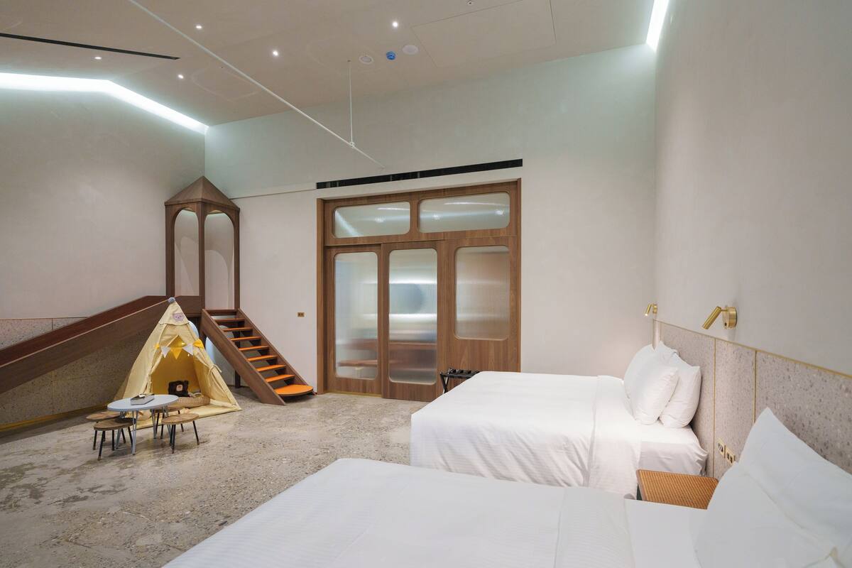 A hotel room with two beds, a small table, a tent, and a staircase.