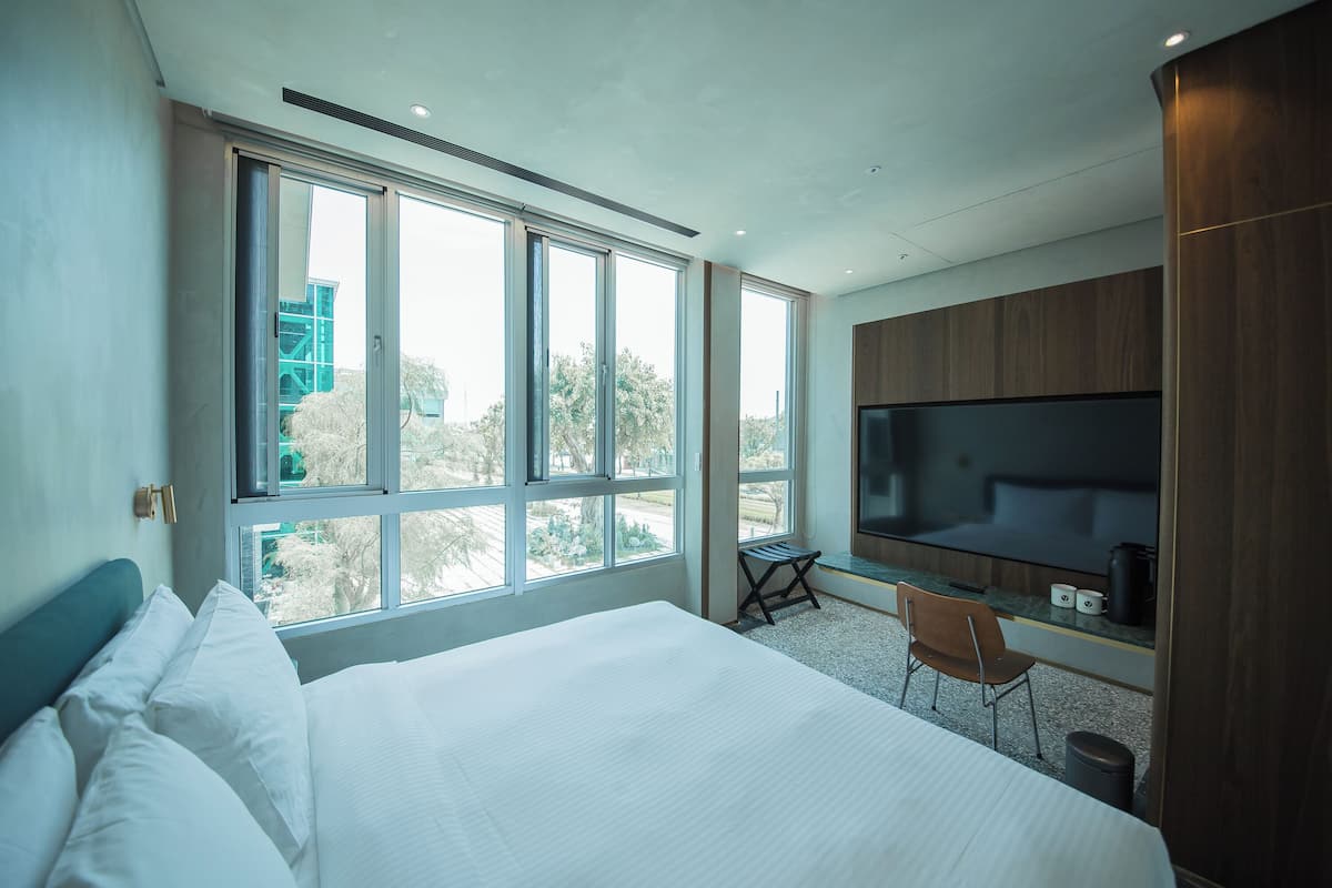 A modern hotel room with a large bed, a desk, a chair, and a TV.