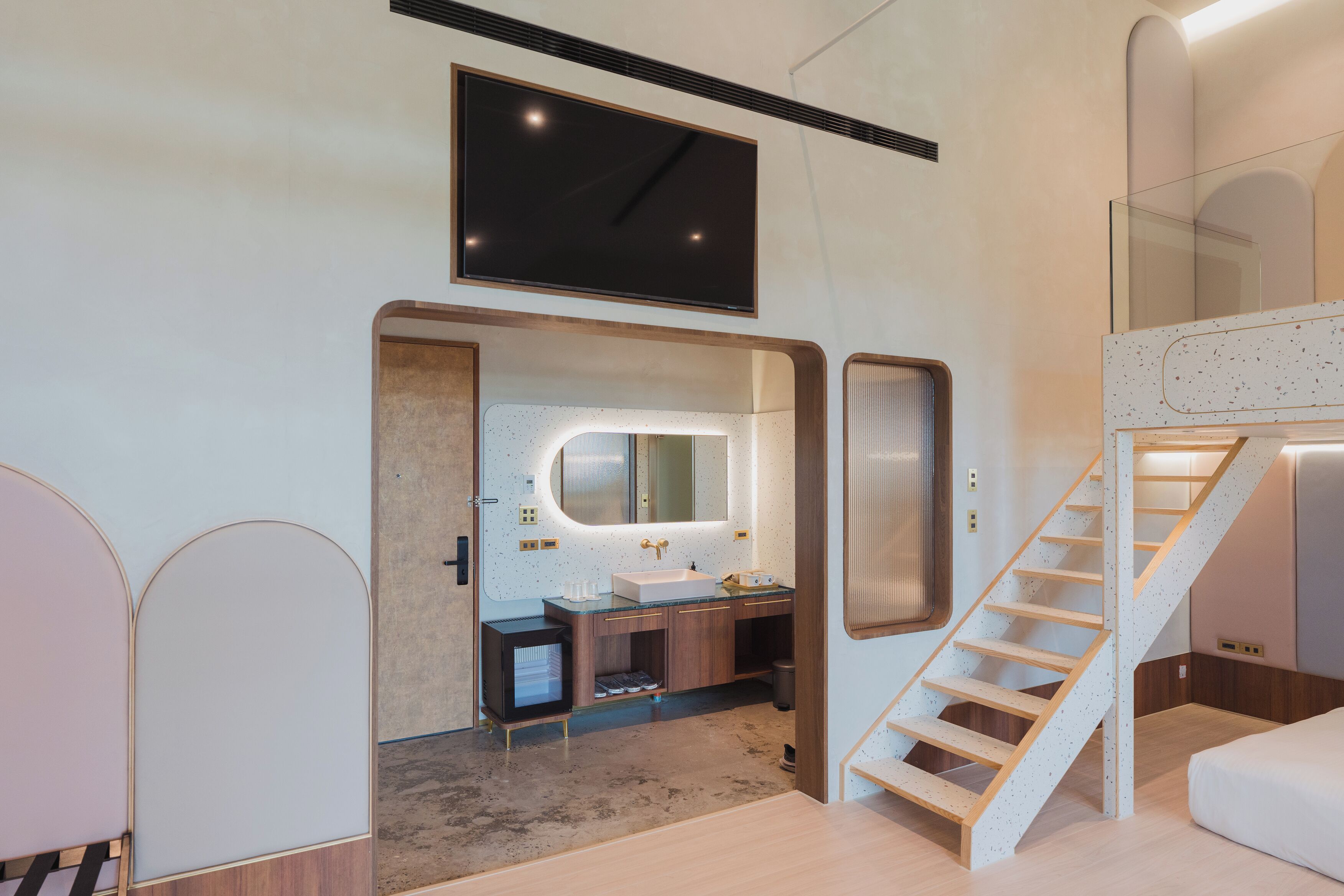 A modern bathroom with a large mirror, a sink, and a shower. There is a staircase leading to an upper level.