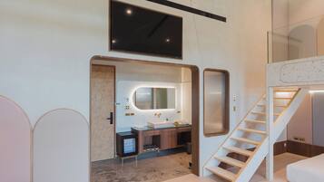 A modern bathroom with a large mirror, a sink, and a shower. There is a staircase leading to an upper level.
