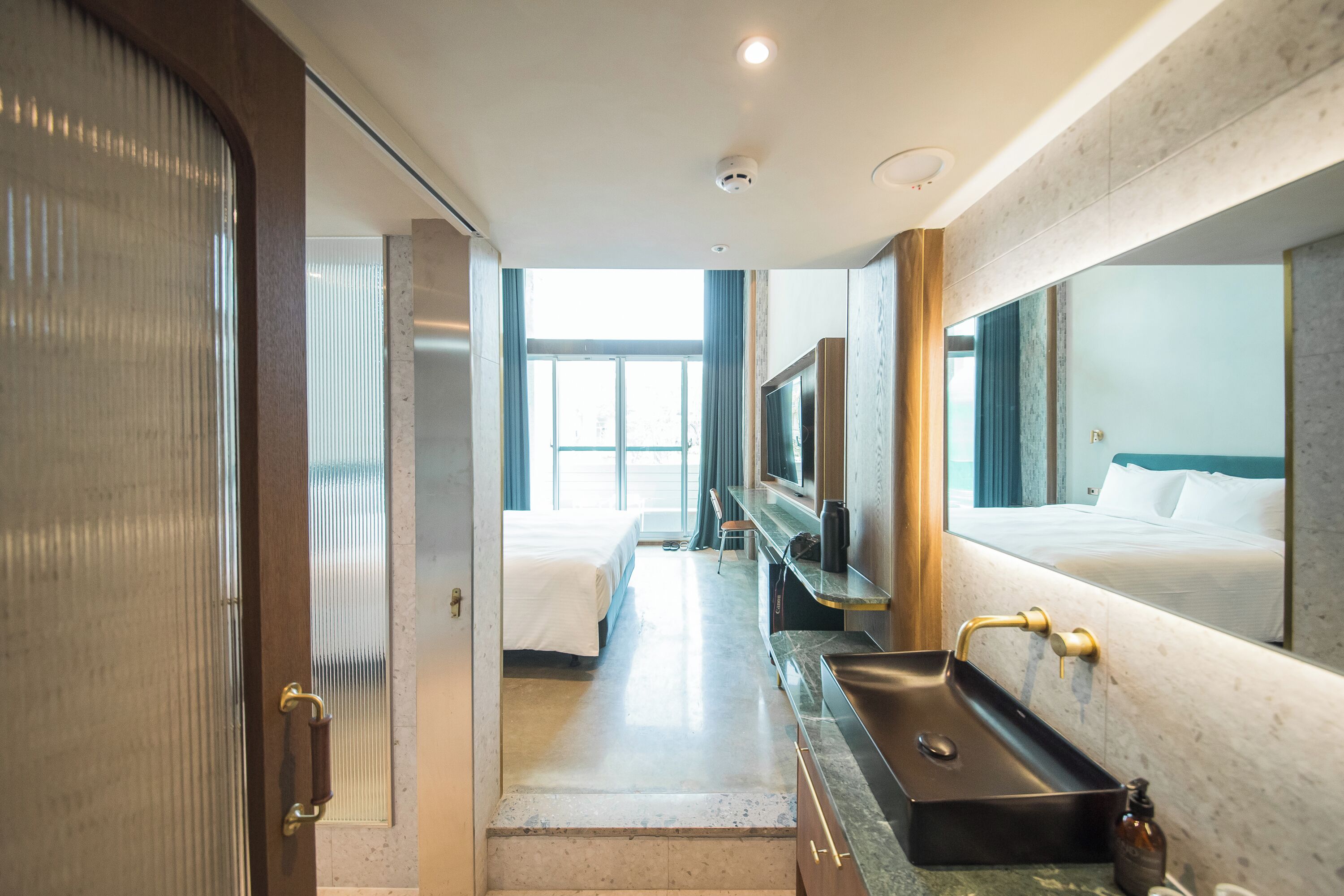 A modern hotel room with a large bed, a bathroom with a sink and mirror, and a TV.