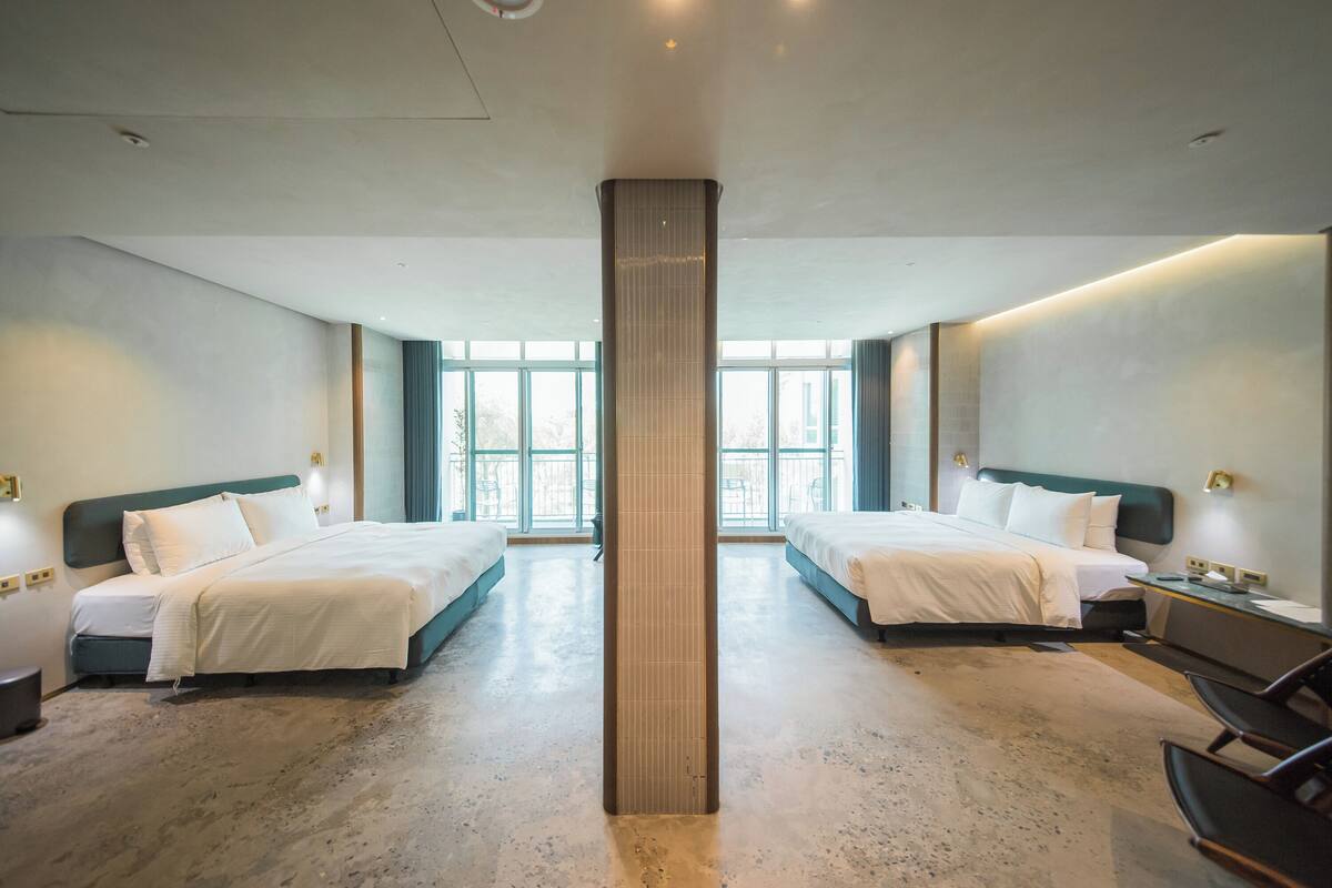 A hotel room with two beds, a large pillar, and a view of the outdoors.