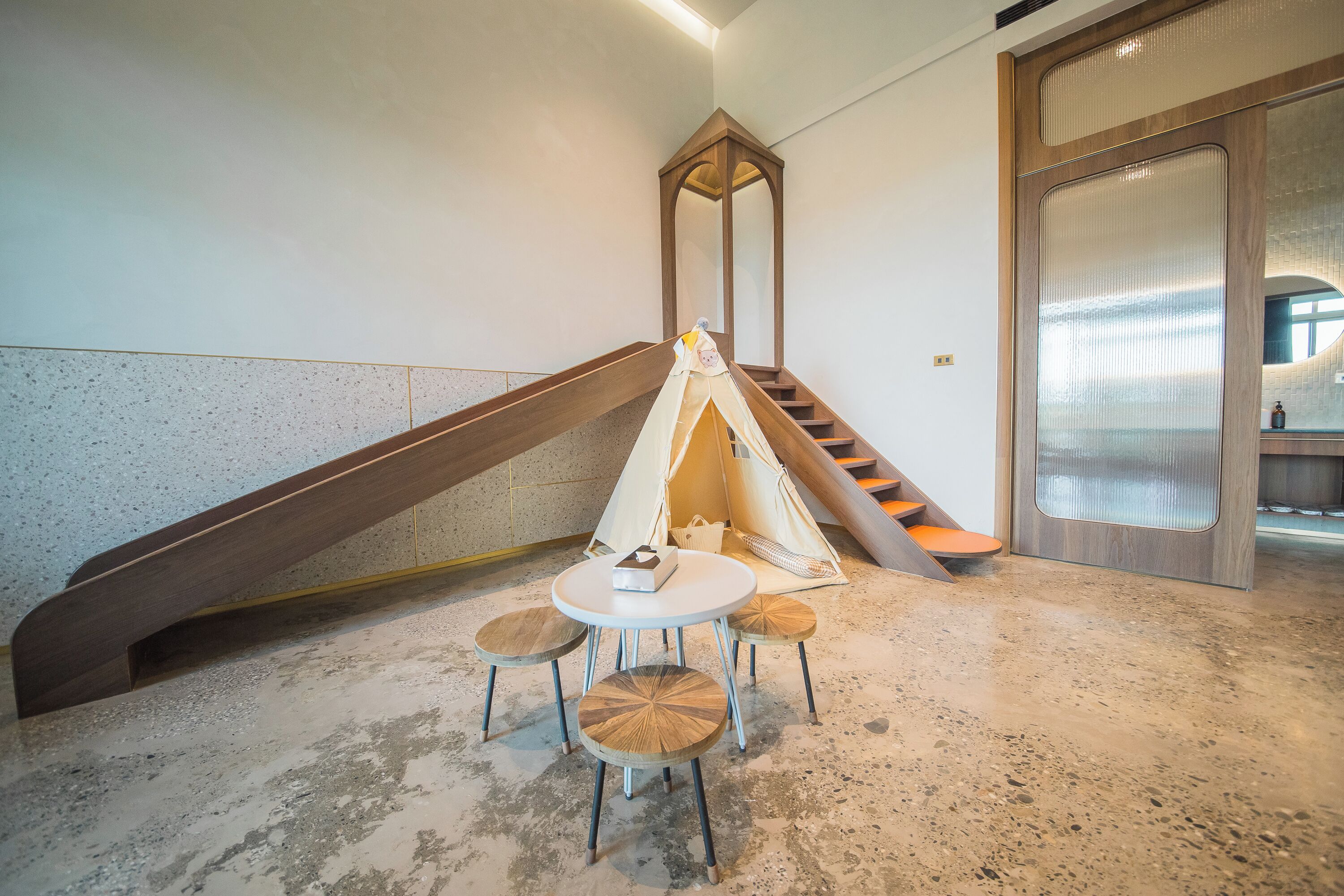 A modern interior with a wooden staircase, a small round table with chairs, and a tent-like structure.