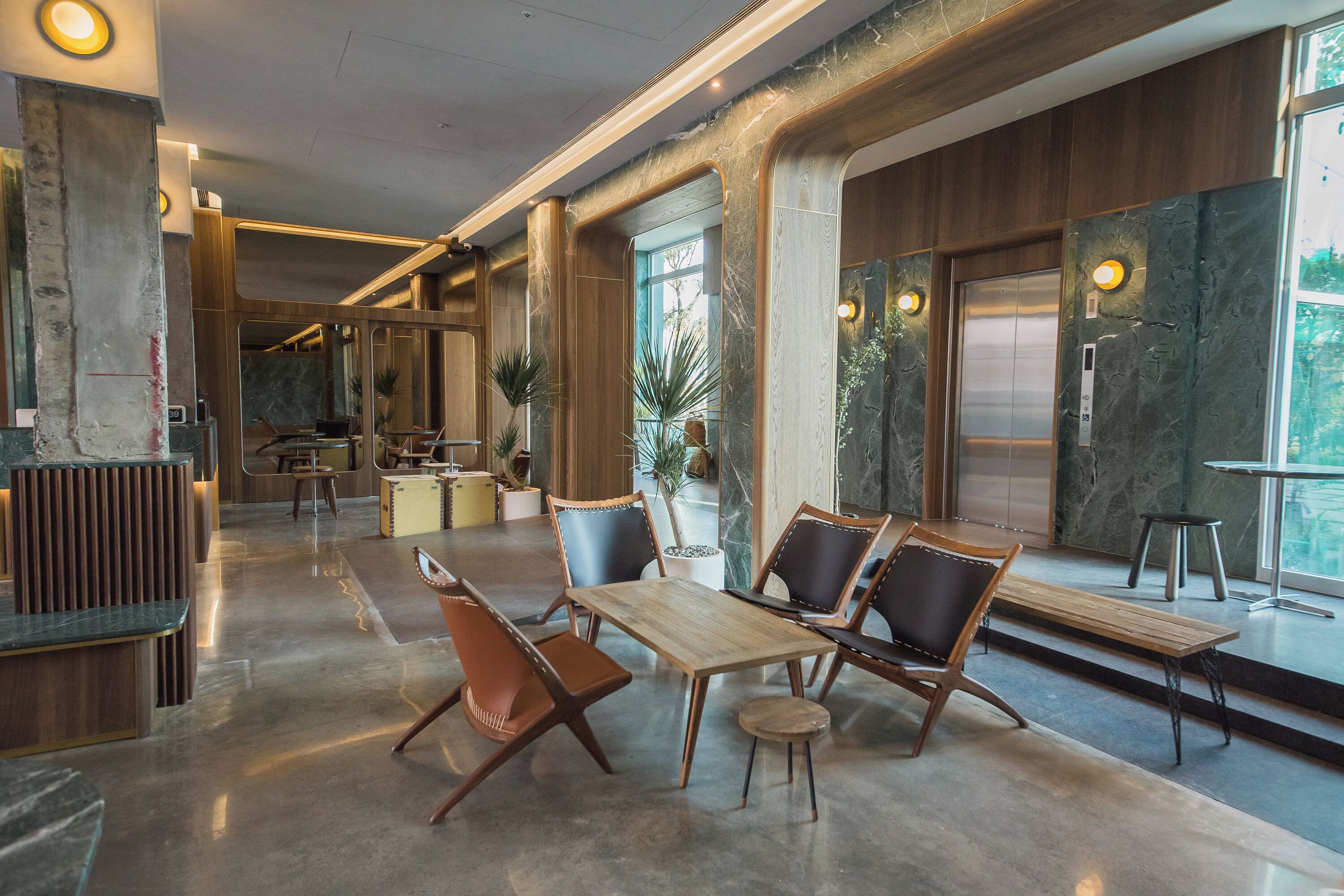A spacious lobby with a marble floor, wooden reception desk, seating area with chairs and a table, and large windows offering a view of the outdoors.
