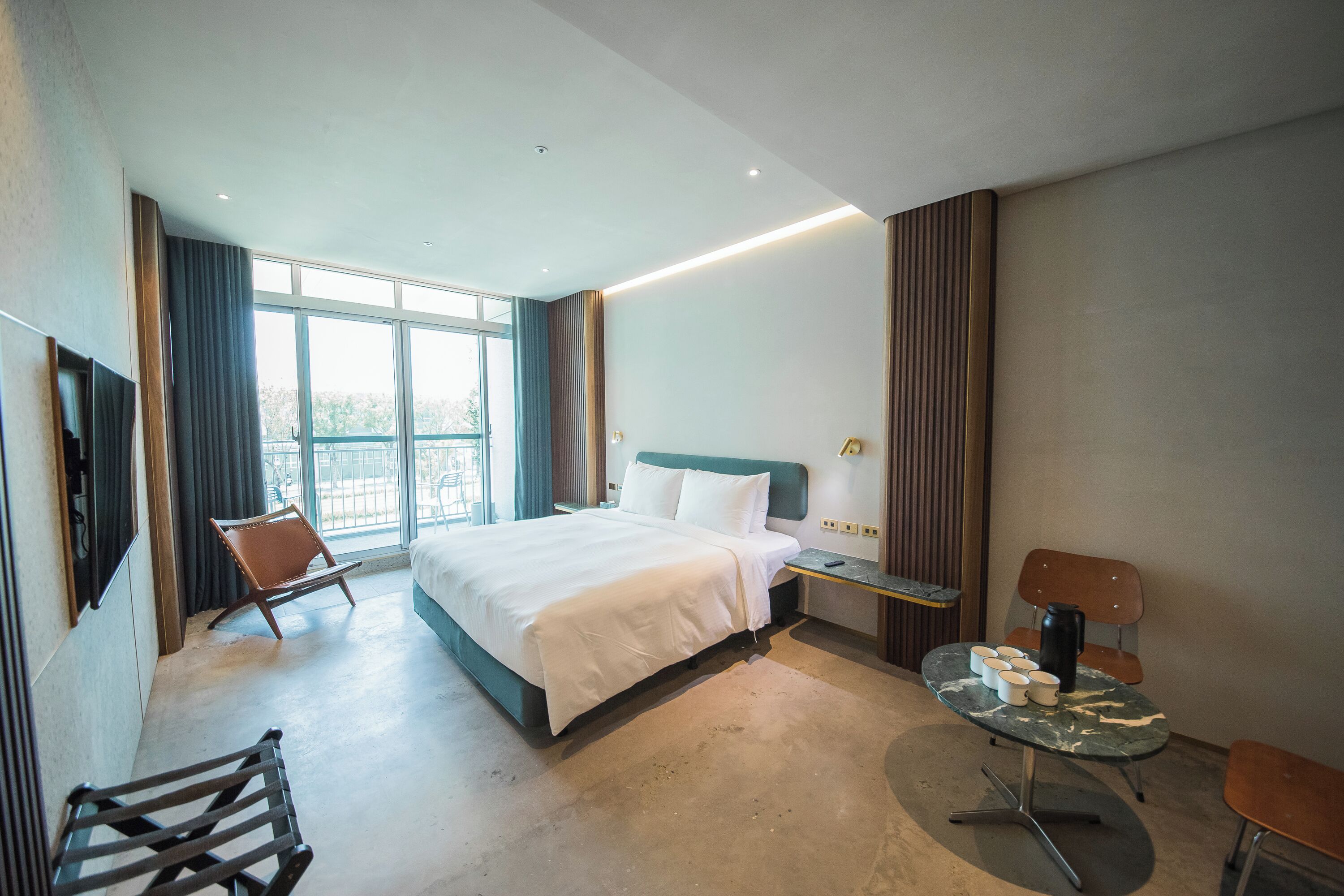 A modern hotel room with a large bed, a desk, a chair, and a small table with cups.