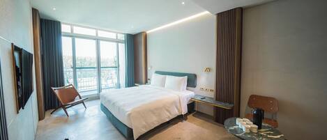 A modern hotel room with a large bed, a desk, a chair, and a small table with cups.
