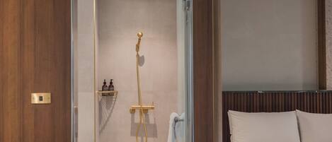A hotel room with a glass shower enclosure, a bed with white linens, and a wooden headboard.