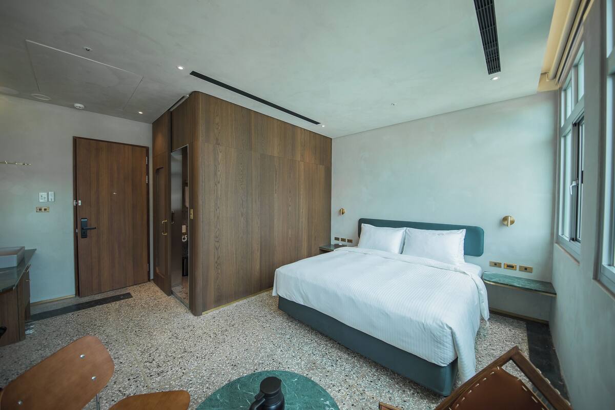 A modern hotel room with a large bed, wooden wardrobe, and a desk with a chair.