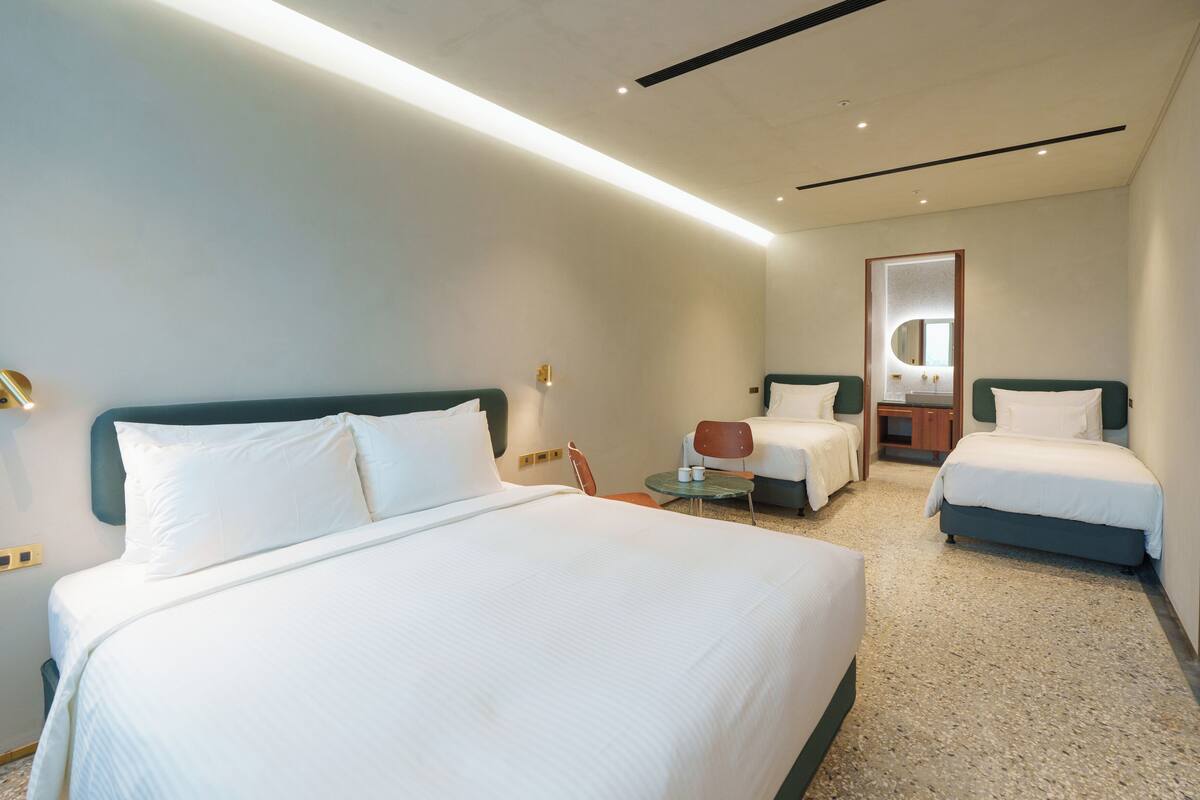 A hotel room with a large bed, two smaller beds, a chair, and a small table.
