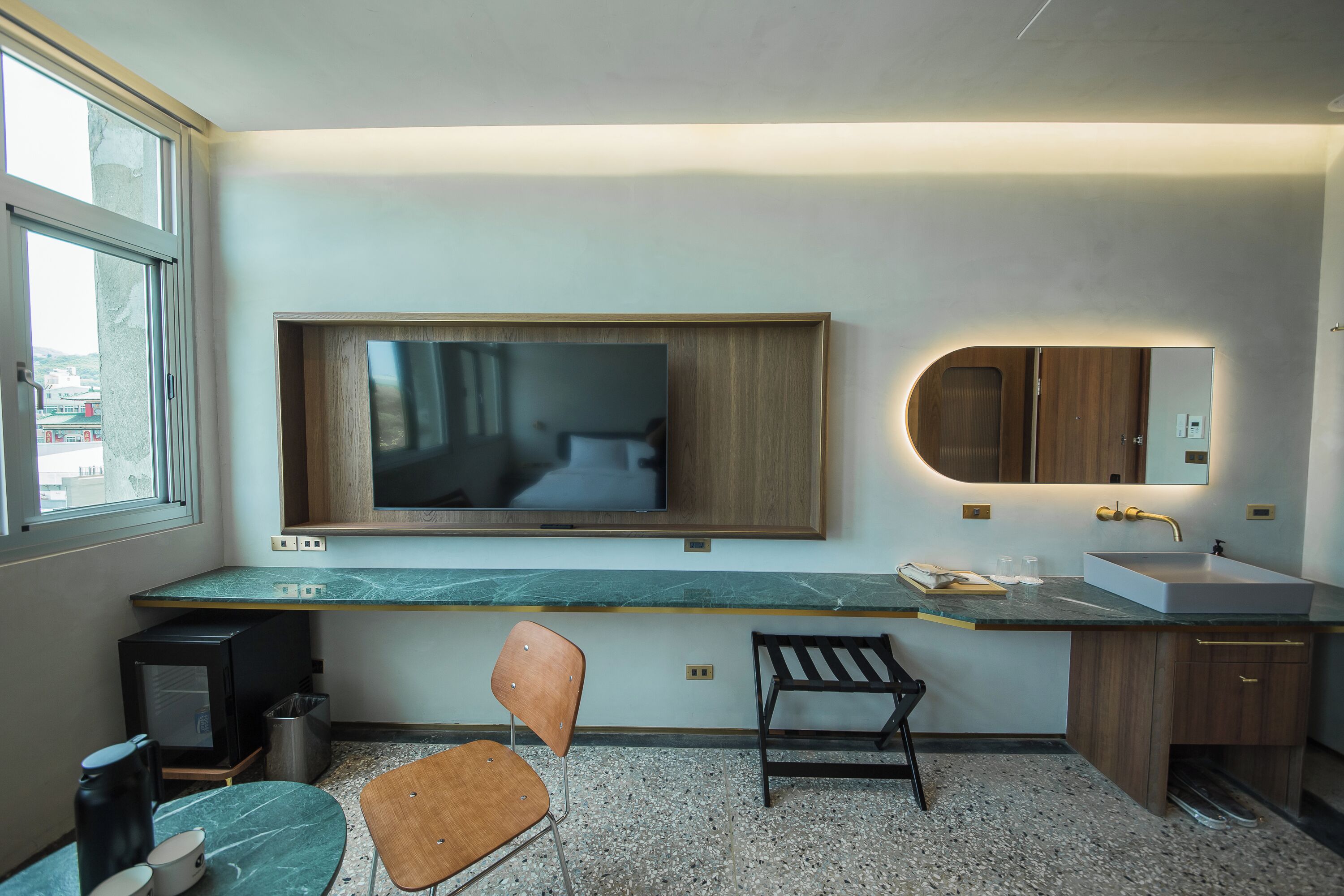 Une salle de bain moderne avec un grand miroir, un lavabo, une chaise et un téléviseur fixé au mur.