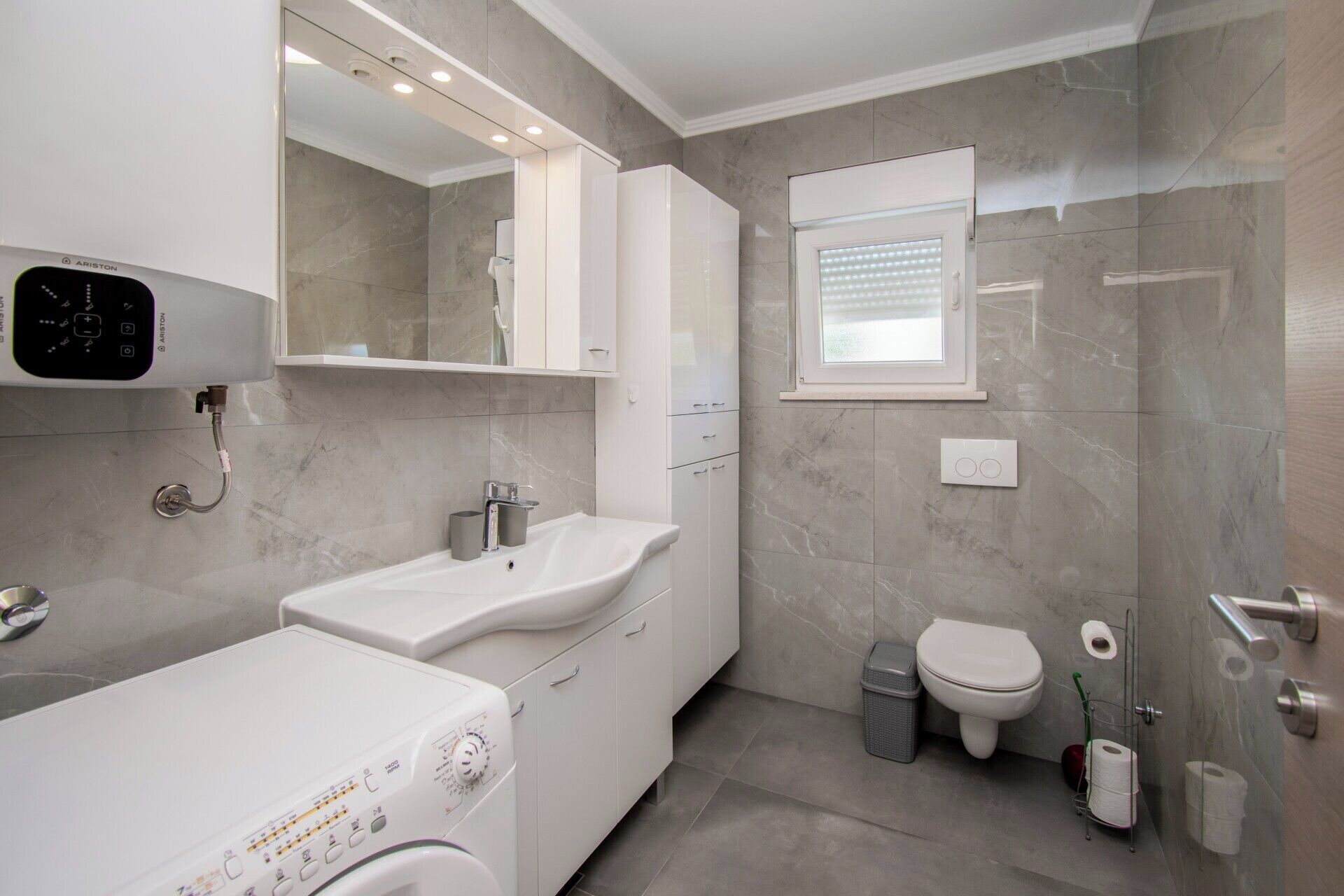 A modern bathroom with a washing machine, a sink, a toilet, and a shower area.