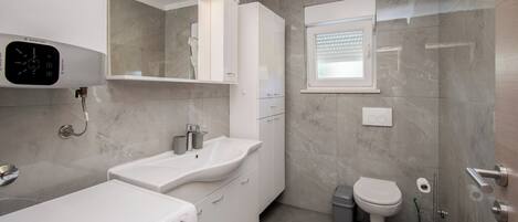 A modern bathroom with a washing machine, a sink, a toilet, and a shower area.