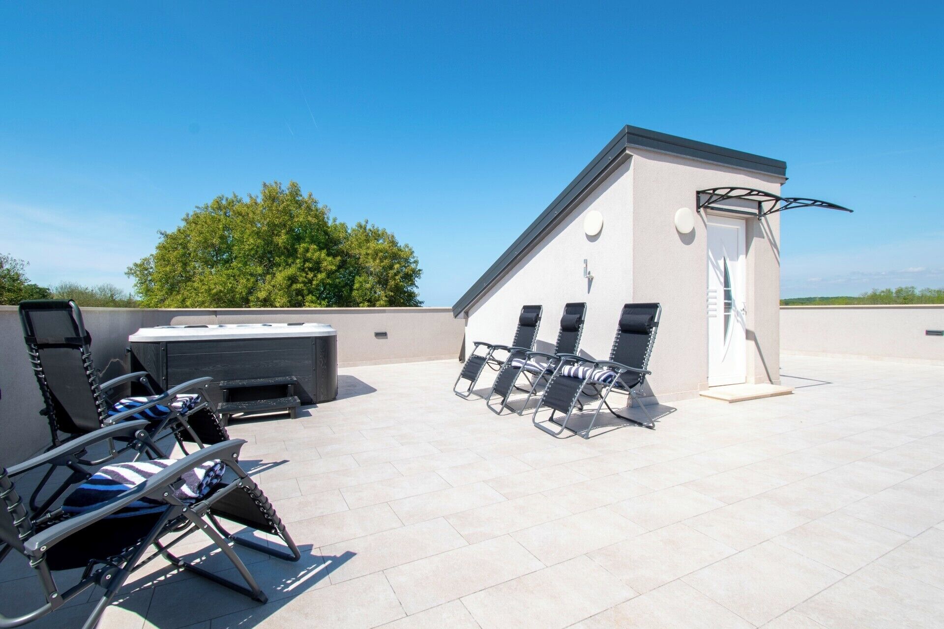 Une terrasse sur le toit équipée d’un jacuzzi, de chaises longues et d’un petit bâtiment doté d’une porte et d’une fenêtre.
