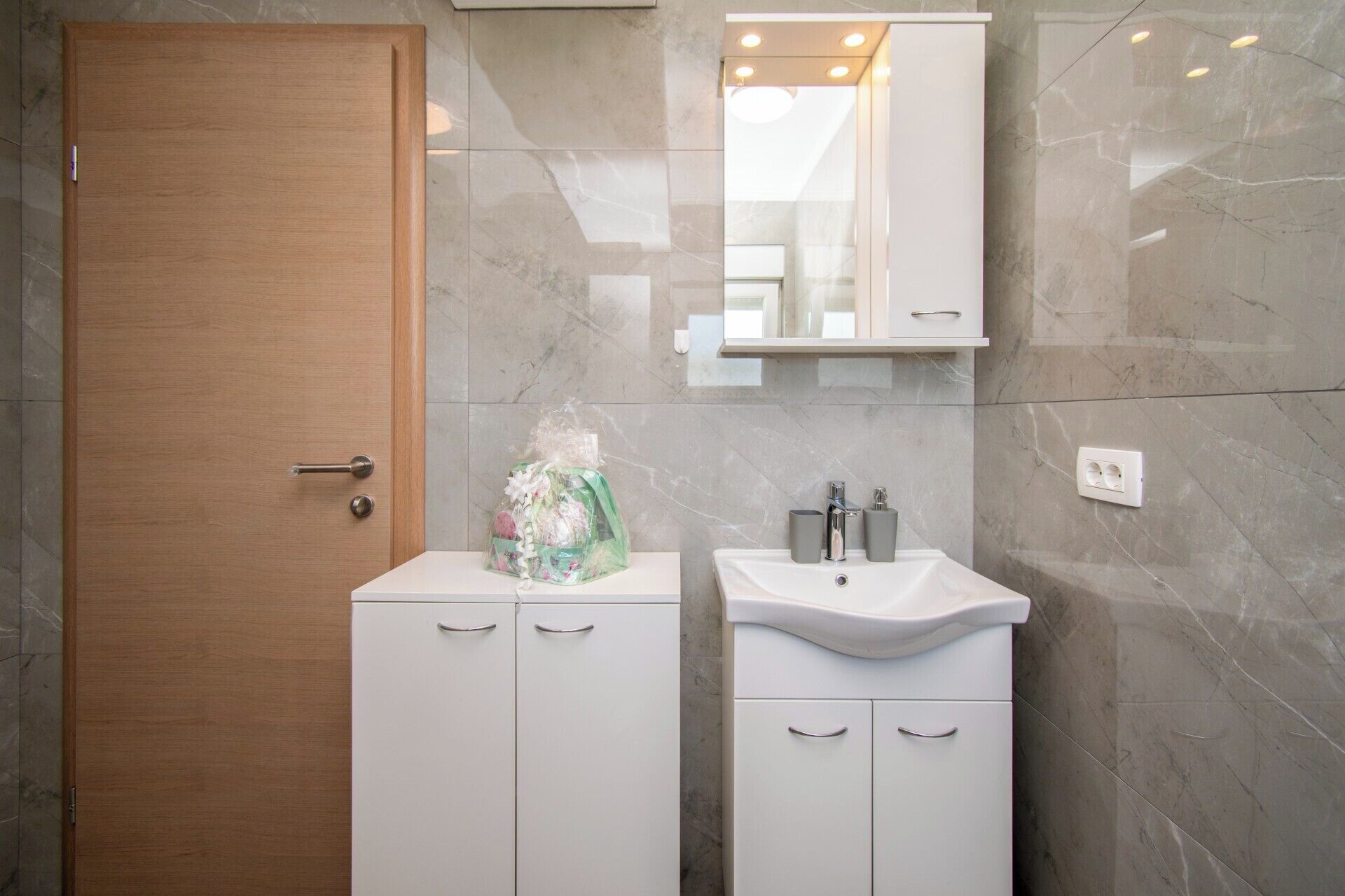 A bathroom with a wooden door, a white sink with a mirror above it, and a small cabinet below.