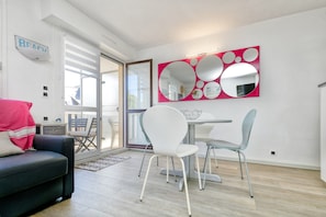 A modern living room with a sofa, a dining table with chairs, a large mirror, and a sliding glass door leading to an outdoor area.