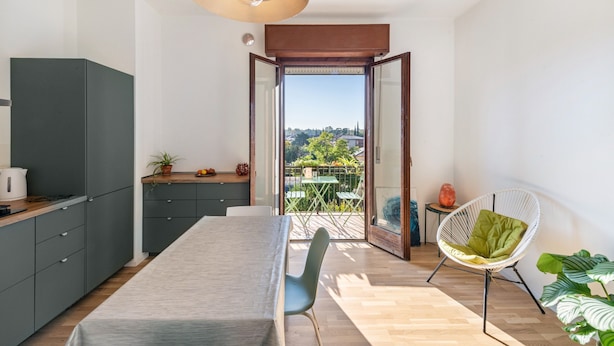 Une cuisine moderne avec un coin repas, une vue à travers une porte ouverte et un espace détente avec un fauteuil.