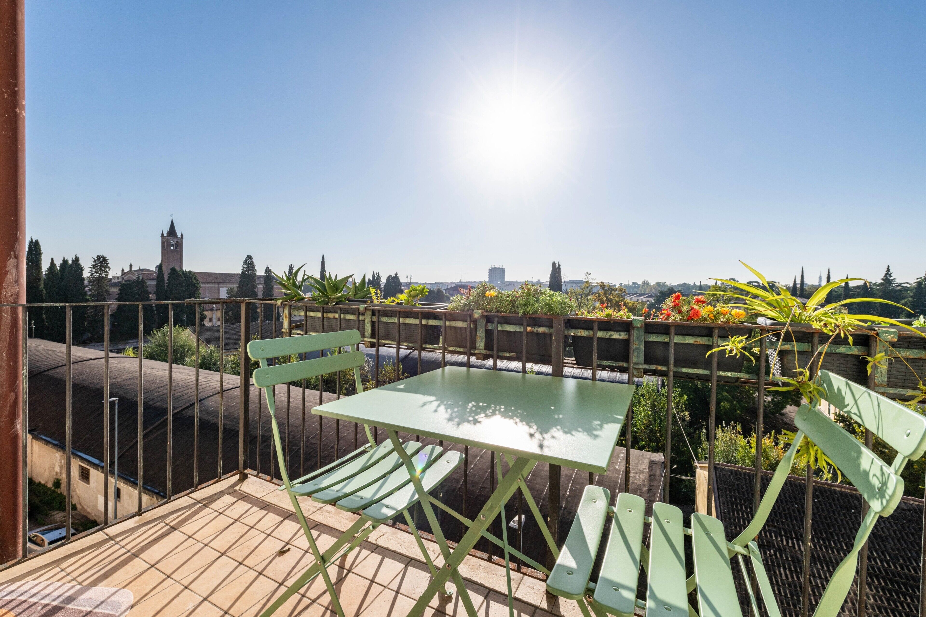 A terrace with a table and chairs, a view of a cityscape, and a clear sky.