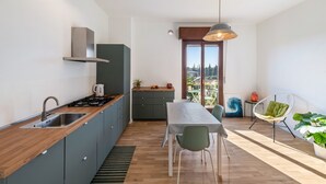 Une cuisine moderne dotée d’une cuisinière intégrée, d’un évier et de placards, un coin repas avec une table et des chaises, et une vue dégagée sur l’extérieur grâce à une grande fenêtre.
