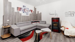 Ein modernes Wohnzimmer mit einem grauen Ecksofa, einem weißen Sessel, einem kleinen weißen Tisch, einem roten und schwarzen Teppich, einem Holzboden, einer Kandelaberleuchte und einem roten und schwarzen Kamin.