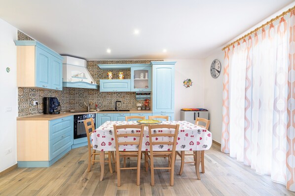 A kitchen with blue cabinets, a dining table with chairs, and a clock on the wall.