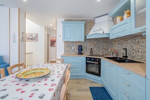 A compact kitchen with light blue cabinets, a patterned backsplash, and a dining area with a table set for two.