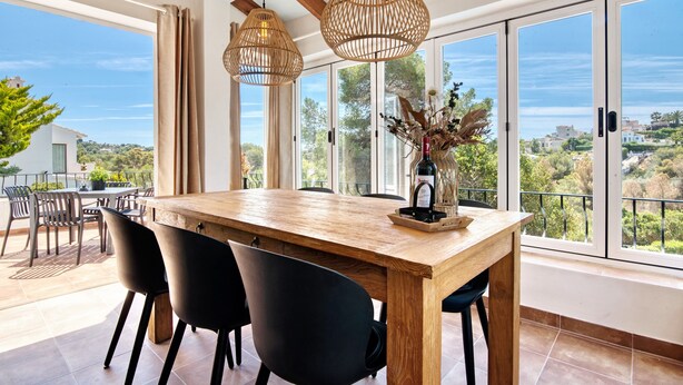 A dining area with a wooden table, black chairs, and large windows with a view of greenery. - Villa 'Casa Crystal' with Mountain View, Wi-Fi and Air Conditioning (Javea)