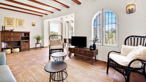 A spacious living area with a television, seating, a wooden ceiling, and large windows. - Villa 'Casa Crystal' with Mountain View, Wi-Fi and Air Conditioning (Javea)