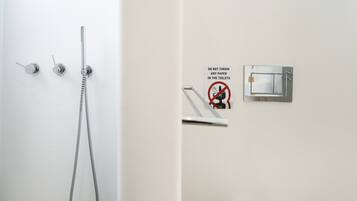 A bathroom with a shower, a toilet, and a sign prohibiting paper disposal in the toilet.