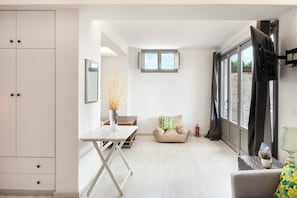 A room with a dining table, a sofa, a window with curtains, and a TV mounted on the wall. - Apartment 'Lavender' with Sea View, Wi-Fi and Air Conditioning (Milos)