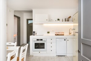 A compact kitchen with white appliances, a dining area with white chairs, and a door leading to another room. - Apartment 'Lavender' with Sea View, Wi-Fi and Air Conditioning (Milos)
