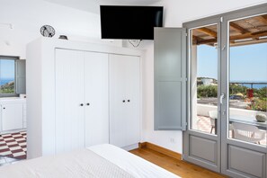 Un dormitorio con cama, televisor, armario y puerta corrediza de vidrio que da a un espacio exterior.